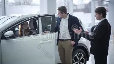 快乐的白种人年轻女人坐在车里，她的丈夫和经销商交谈。 成<strong>功夫</strong>妇购买车辆